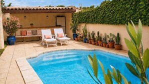 Uma piscina com espreguiçadeiras, um banco e plantas em vasos.