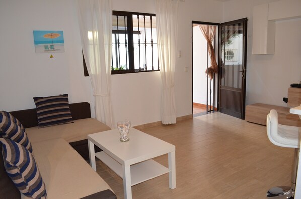 Uma sala de estar com sofá, mesa de centro e porta que dá para outro cômodo.
