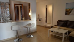 Uma sala de estar moderna com um sofá branco, dois bancos altos brancos, uma mesa de centro branca e um espelho sobre o balcão.