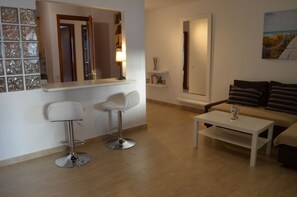 Ein modernes Wohnzimmer mit einem weißen Sofa, zwei weißen Barhocker, einem weißen Couchtisch und einem Spiegel über der Theke.