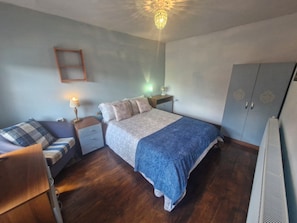 A bedroom with a bed, a nightstand, a lamp, a wardrobe, and a ceiling light fixture.