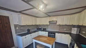 Eine kleine Küche mit weißen Schränken, einem Holztisch, einem Hocker, einer Mikrowelle, einem Toaster und einem Wasserspender.