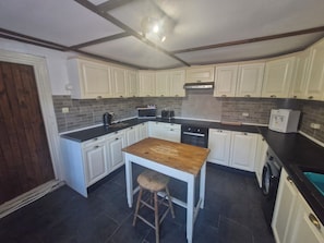 A compact kitchen with white cabinets, a wooden table, a stool, a microwave, a toaster, and a water dispenser.