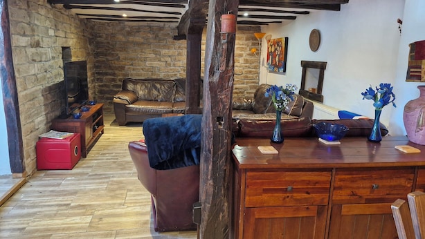 Ein rustikales Wohnzimmer mit sichtbaren Holzbalken, einem Kamin aus Stein, Ledersofas und einem Holzkabinett.