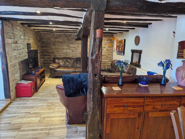 A rustic living room with exposed wooden beams, a stone fireplace, leather sofas, and a wooden cabinet.