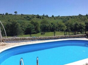 A swimming pool with a stone border, surrounded by a grassy area and trees.