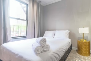 Ein Hotelzimmer mit einem ordentlich bezogenen Bett, einem Fenster mit Vorhängen und einer Nachttischlampe.