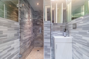Ein modernes Badezimmer mit Duschkabine aus Glas, einem weißen Waschbecken und einer gefliesten Rückwand.