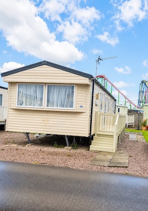 A mobile home with a number 50, a small porch, and a roller coaster in the background.