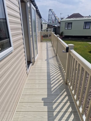 Une terrasse en bois avec une rambarde blanche, qui mĂšne Ă un bĂątiment dotĂ© dâune porte-fenĂȘtre coulissante.