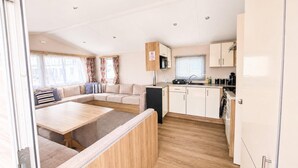 A compact RV interior with a kitchenette, a dining area, and a seating area with a sofa. - 3 Bed Caravan - Sleeps 8 - Free Parking (Skegness)