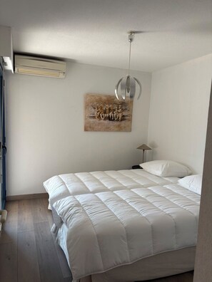 A bedroom with a large bed, a ceiling fan, an air conditioning unit, and a wall-mounted artwork. - Vrbo Property (Cavalaire-sur-Mer)