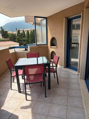 A balcony with a table and chairs, a view of buildings and trees, and a door with a glass panel. - Vrbo Property (Cavalaire-sur-Mer)