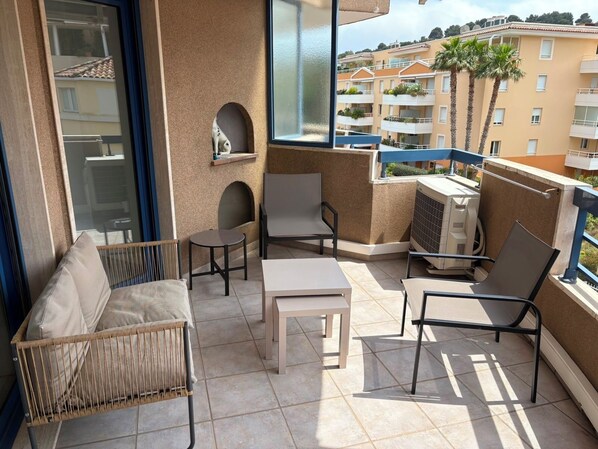 A balcony with a sofa, chairs, a table, and a small shelf. - Vrbo Property (Cavalaire-sur-Mer)