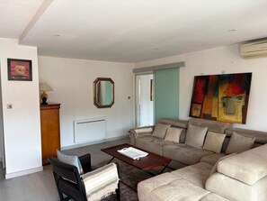 A living room with a sofa, a coffee table, a lamp, a mirror, and a painting. - Vrbo Property (Cavalaire-sur-Mer)