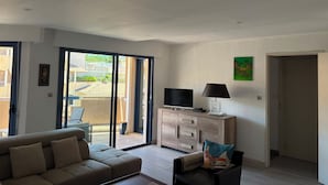 Una sala de estar con un sofá, un televisor, un armario y un ventanal corredizo que da a un espacio exterior.