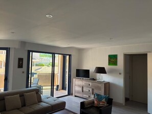A living room with a sofa, a TV, a cabinet, and a sliding glass door leading to an outdoor area. - Bright apartment on 3ᵉ floor - 2 bedrooms and 2 bathrooms (Cavalaire-sur-Mer)