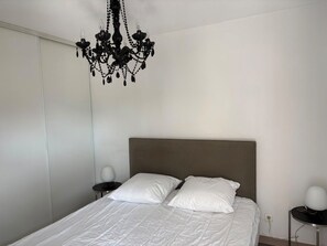 Ein Schlafzimmer mit einem Bett, weißen Kissen, einer Chandelier, einem Nachttisch und einer Wandlampe.