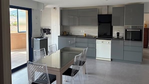 Una cocina moderna con armarios grises, una campana extractora negra, un horno empotrado y una zona de comedor con una mesa de vidrio y sillas.
