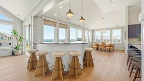 A spacious kitchen with a large island, bar stools, and a view of the ocean.