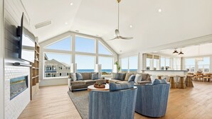 A spacious living room with a large window overlooking the ocean, a fireplace, and a ceiling fan.