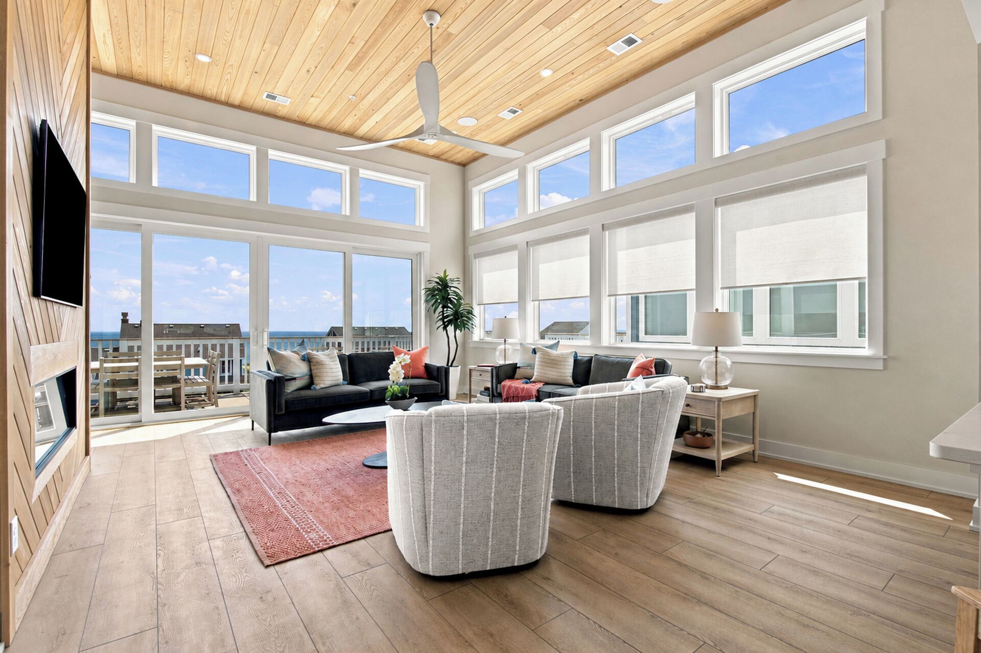 A spacious living room with a high ceiling, large windows, and a view of the sea.