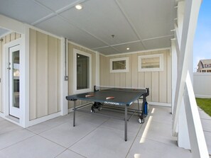 An outdoor ping pong table with wheels, set on a tiled patio with a white wall and windows. - BRAND NEW Luxury Semi-Oceanfront in Kill Devil Hills Seaduction (Kill Devil Hills)