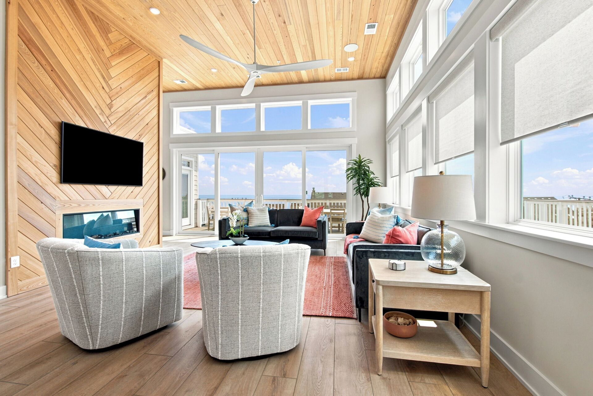 A spacious living area with a ceiling fan, large windows, and a view of the sea.
