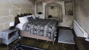 Ein rustikales Schlafzimmer mit einem hölzernen Bett, einer Steinwand und einem kleinen Rundbogen.