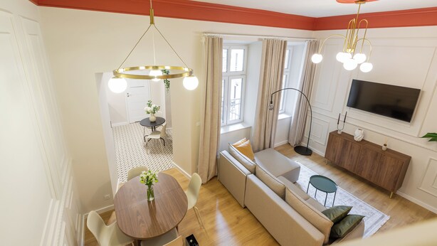 Una sala de estar moderna con un sofá, una mesa de comedor con sillas, un televisor montado en la pared y un ventilador de techo.