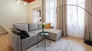 Una sala moderna con un sofá seccional gris, una mesita redonda con un jarrón y una lámpara de pie.