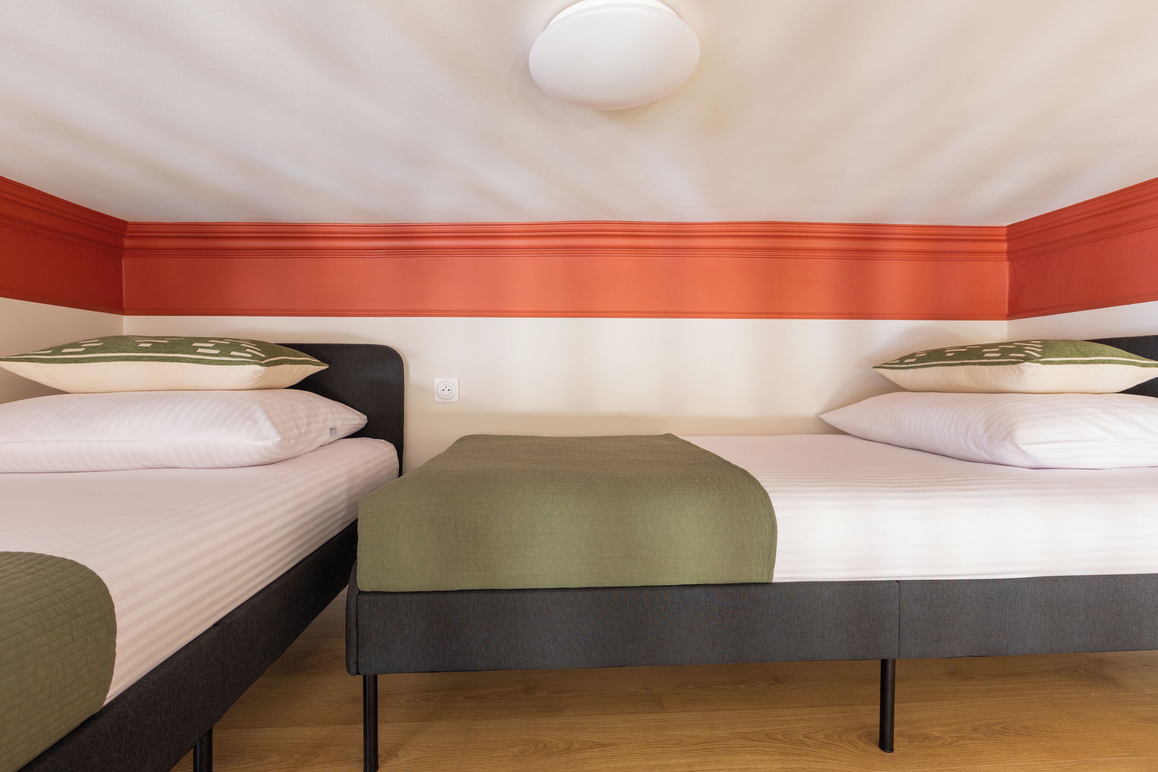 A room with two beds, a single light fixture, and a power outlet on the wall.
