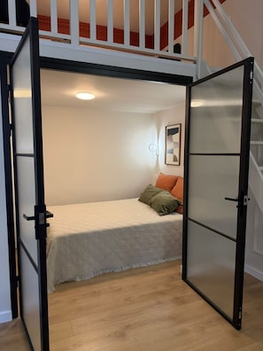 A bedroom with a bed, pillows, a painting, and a staircase. - Native Apartments Węgierska 10  (Kraków)