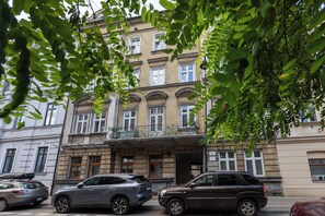Un edificio de varios pisos con balcón, coches aparcados y un árbol en primer plano.