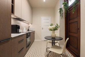 A compact kitchen with modern appliances, a dining table with a vase of flowers, and a patterned floor. - Native Apartments Węgierska 10  (Kraków)