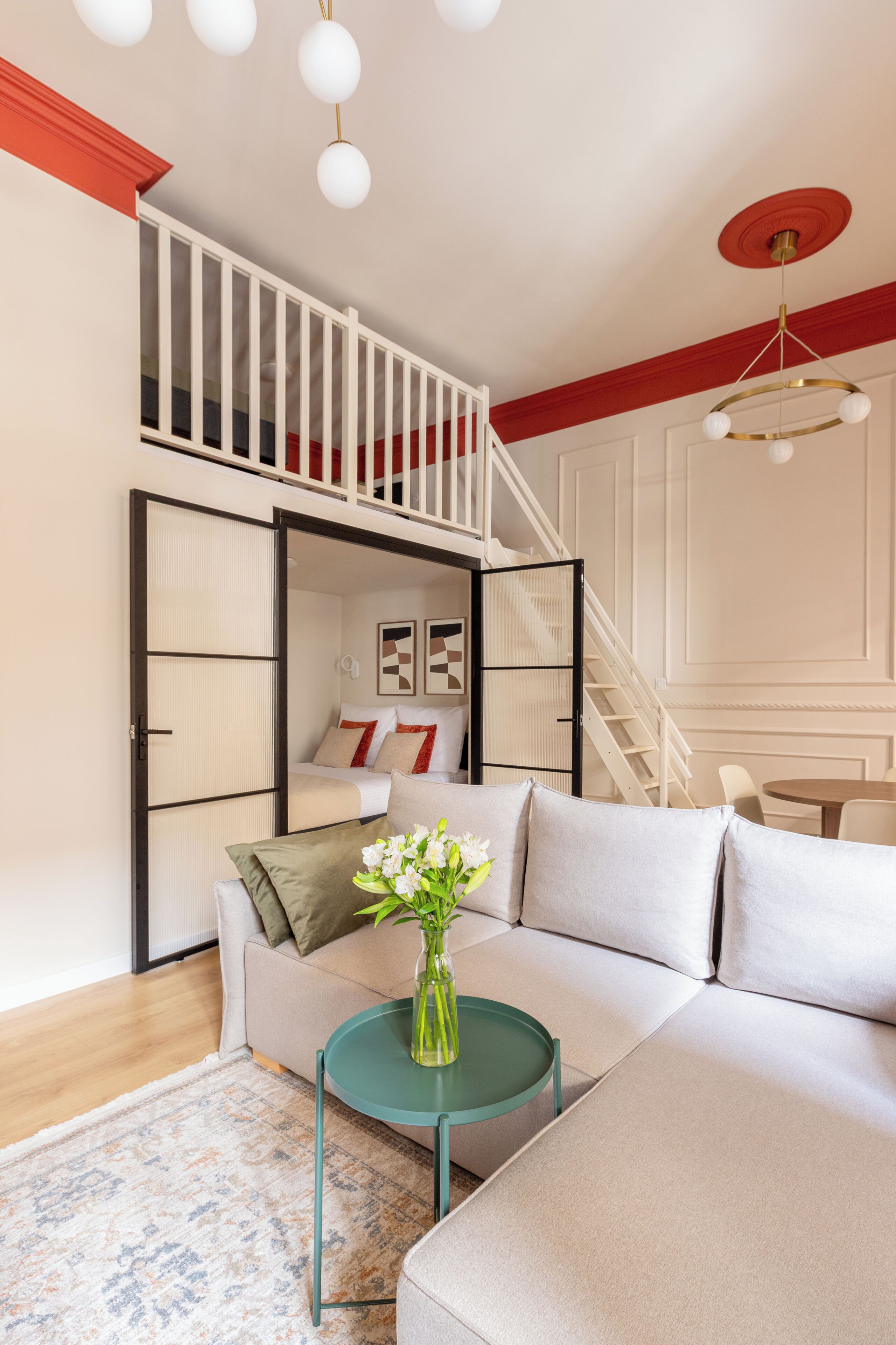 A modern living room with a sectional sofa, a small round table with a vase, a staircase leading to a loft, and a dining area.