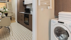 Zona de lavandería con lavadora, un tendedero y una peque ña cocina equipada con refrigerador y horno.