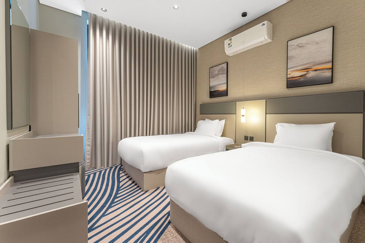 Habitación de hotel con dos camas, un espejo grande, un equipo de aire acondicionado y un cuadro en la pared.