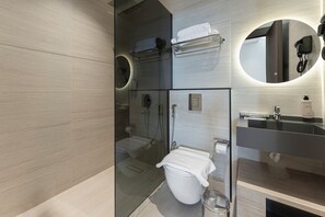 Et moderne badeværelse med en glasafskærmet brusekabine, toilet, vask og et spejl med telefon.