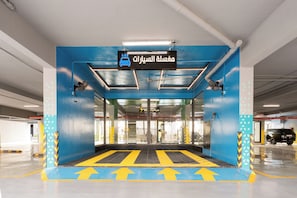 A parking garage entrance with a blue and yellow color scheme, directional arrows on the floor, and a sign with Arabic text. - Lafeef Apartments Al-Namuzji (Madinah)