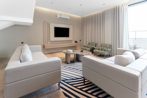 Uma sala de estar moderna com uma TV de tela plana, dois sofás, uma mesa de centro e um tapete estampado.