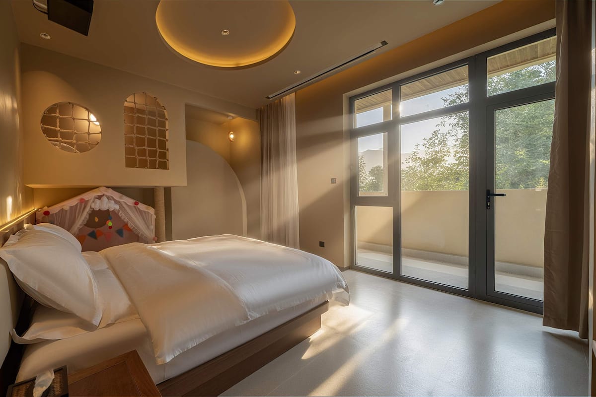 A bedroom with a large bed, a ceiling light, a window, and a door.