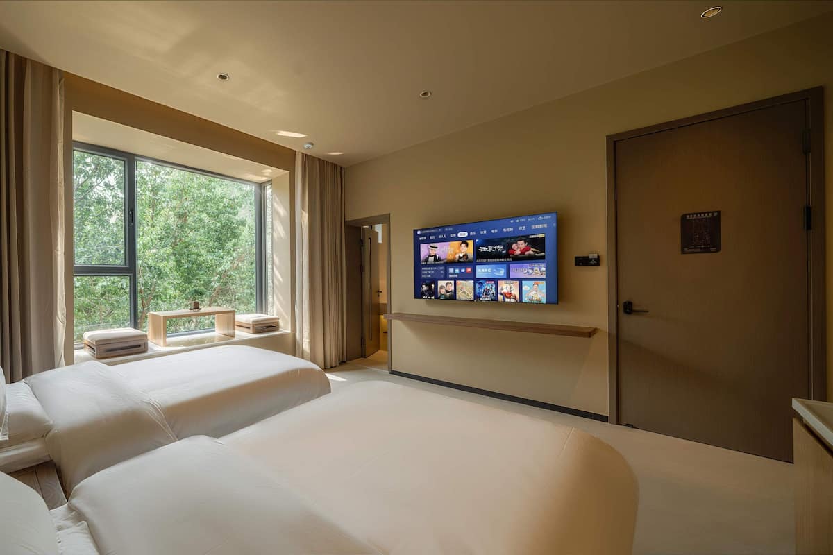 A hotel room with a large bed, a TV mounted on the wall, and a window with curtains.