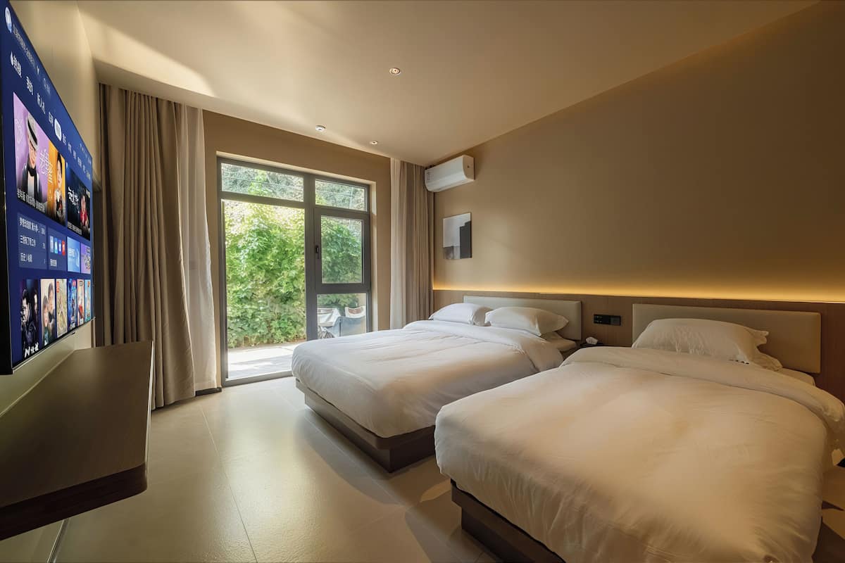 A hotel room with two beds, a TV, and a large window.
