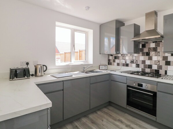 A modern kitchen with grey cabinets, a stainless steel range hood, a built-in oven, and a window providing natural light. - Beacon View (Malvern)