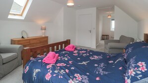 A bedroom with a sloped ceiling, a skylight, a wooden dresser, a bed with a floral duvet, a grey sofa, and a small table. - Beacon View (Malvern)