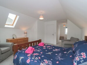 A bedroom with a sloped ceiling, a skylight, a wooden dresser, a bed with a floral duvet, a grey sofa, and a small table. - Beacon View (Malvern)