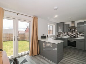A modern kitchen with a large island, sliding glass doors to a backyard, and a view of a residential area. - Beacon View (Malvern)