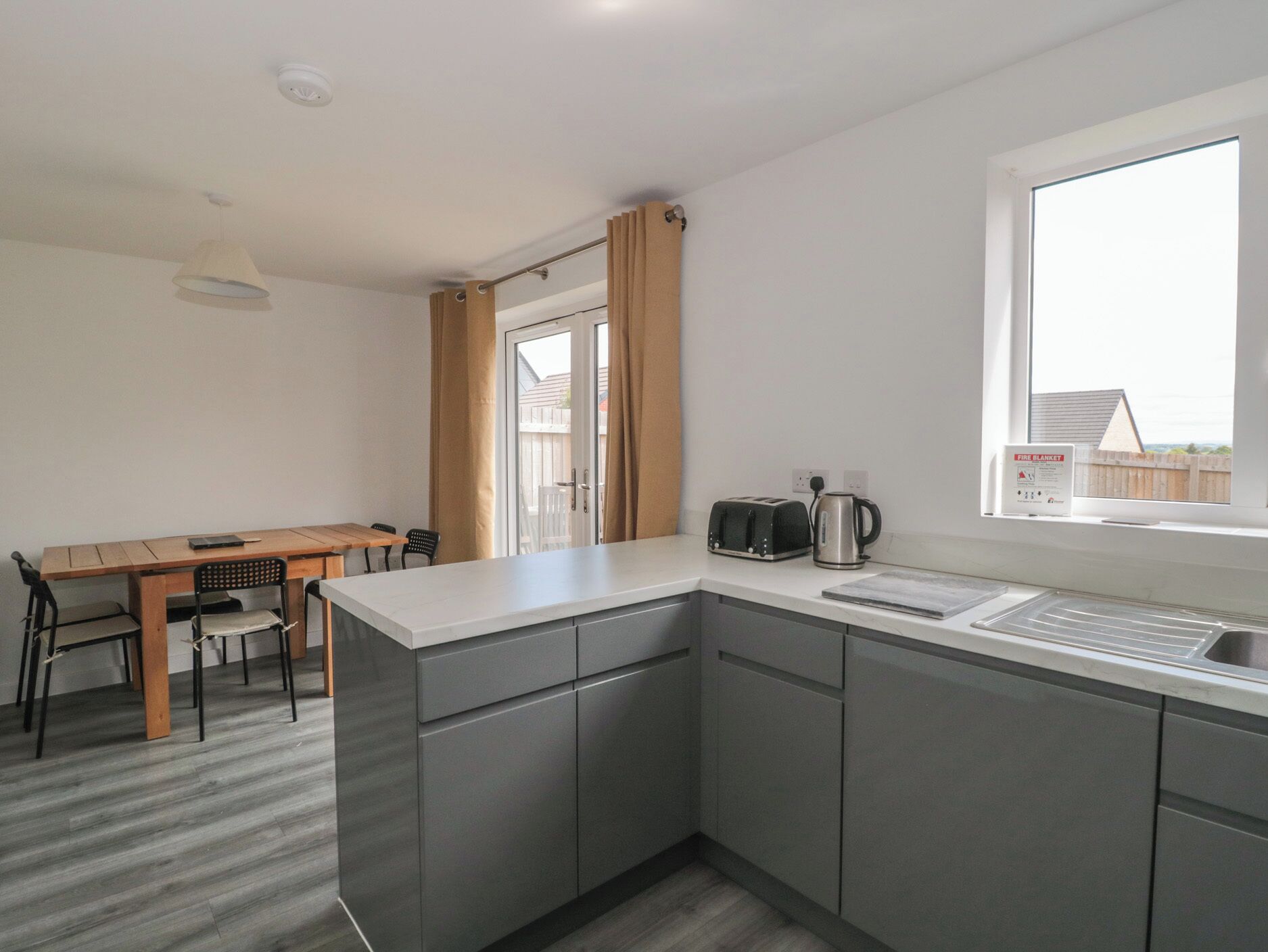 A modern kitchen with grey cabinets, a wooden dining table, and a window with a view of a house.