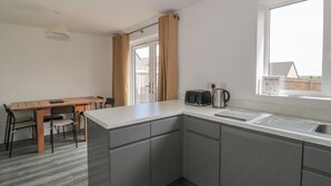 A modern kitchen with grey cabinets, a wooden dining table, and a window with a view of a house. - Beacon View (Malvern)